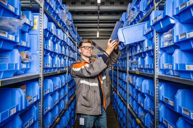 Medewerker pakt een blauwe bak met onderdelen uit de stelling