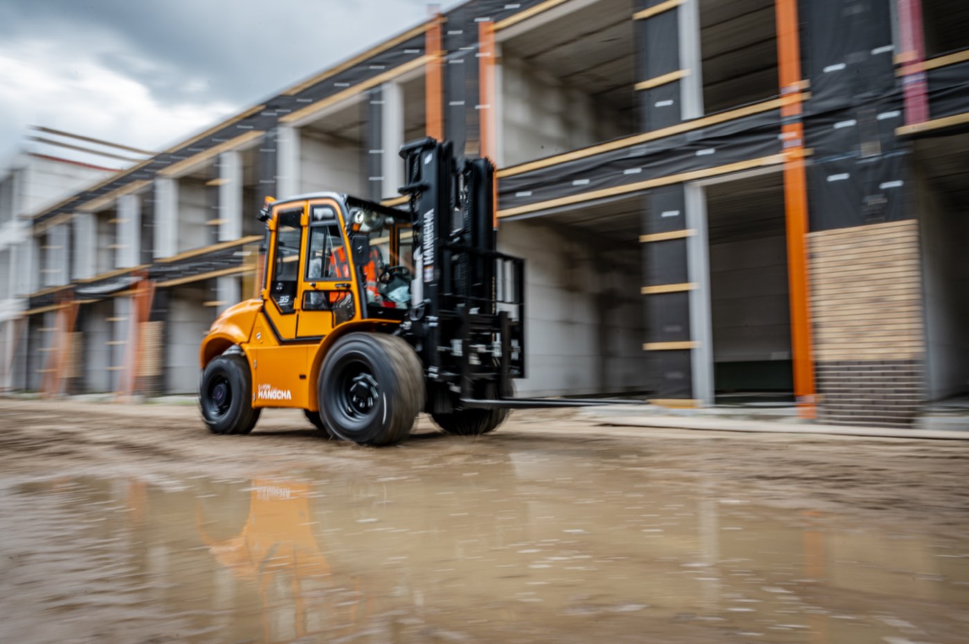 Oranje elektrische Hangcha RT ruwterreinheftruck met 4-wielaandrijving op een nat buitenterrein