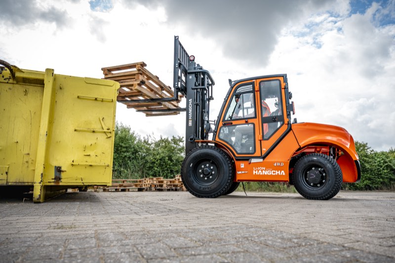 Oranje Hangcha ruwterreinheftruck tilt pallets naast een gele container