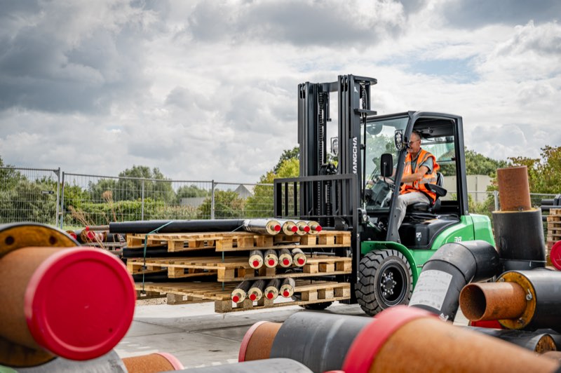 Groene elektrische Hangcha XE heftruck buiten tussen stapels leidingen